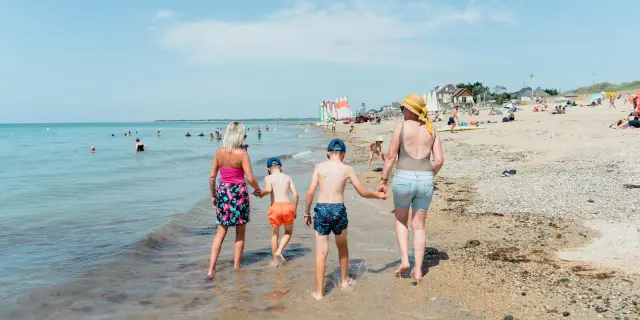 Une famille marche le long de la plage avec deux enfants entre les parents