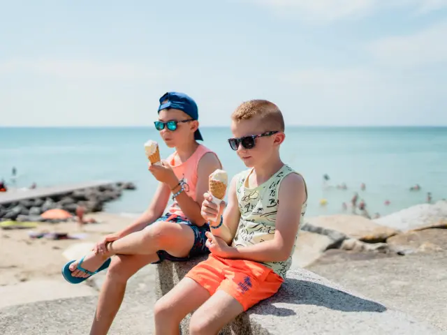 Deux enfants assis sur un rocher au bord de la mer, mangeant des glaces