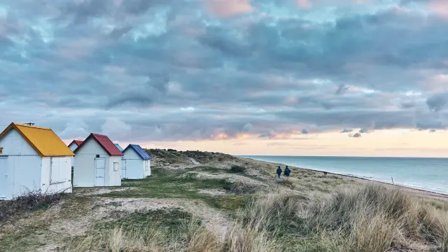 Bunte Strandhütten in einer Reihe auf einer grasbewachsenen Düne am Meer