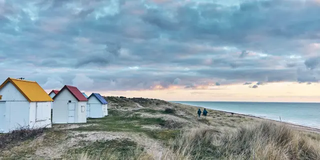 Bunte Strandhütten in einer Reihe auf einer grasbewachsenen Düne am Meer