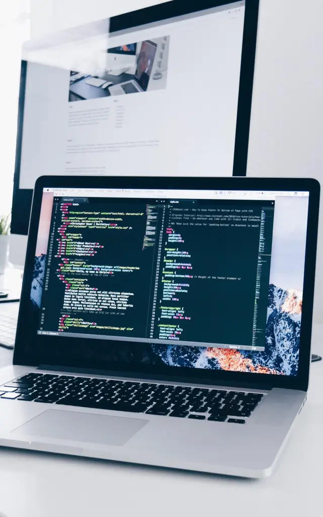Un bureau avec un ordinateur portable affichant du code, un téléphone, des écouteurs et une tasse de café