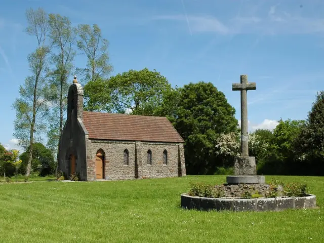 Steinkapelle mit einem Granitkreuz auf einer grünen Wiese