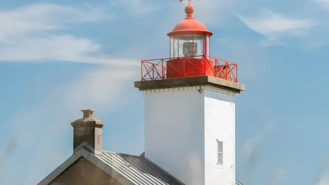 White lighthouse with a red lantern and an adjacent house