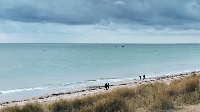 Plage avec des personnes marchant le long de la côte sous un ciel nuageux : fond d'écran