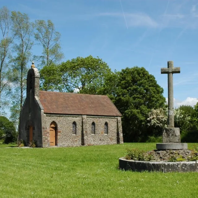 Stone chapel with a granite cross on a green lawn
