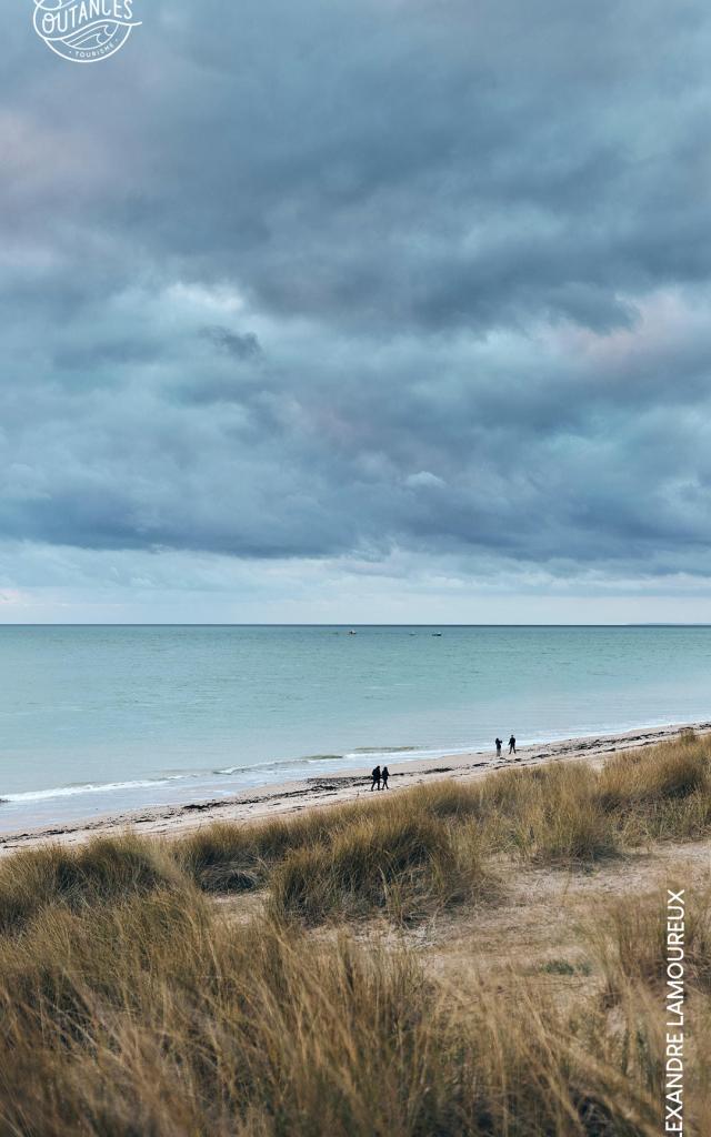 Plage avec des personnes marchant le long de la côte sous un ciel nuageux : fond d'écran