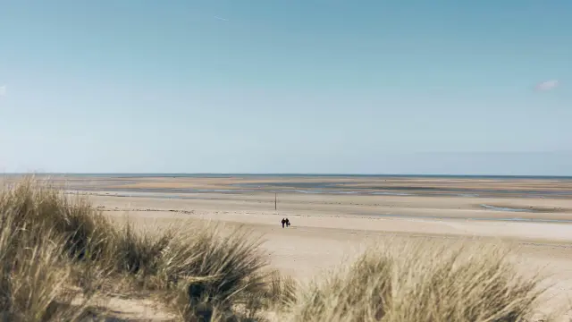 Deux personnes marchant sur une plage de sable avec une mer calme en arrière-plan : plage de Montmartin sur Mer