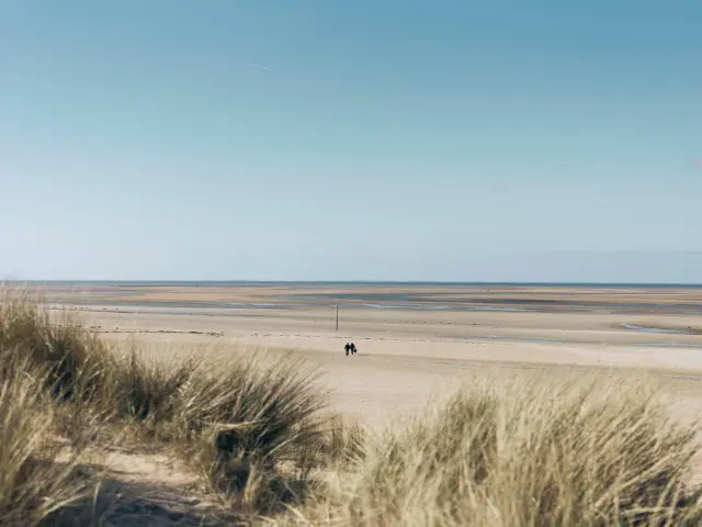 Deux personnes marchant sur une plage de sable avec une mer calme en arrière-plan : plage de Montmartin sur Mer