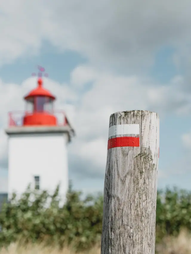White lighthouse with a red roof and a wooden post marked with a red and white stripe