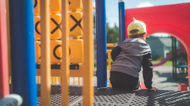 Un enfant portant un chapeau jaune est assis au sommet d'un toboggan dans une aire de jeux
