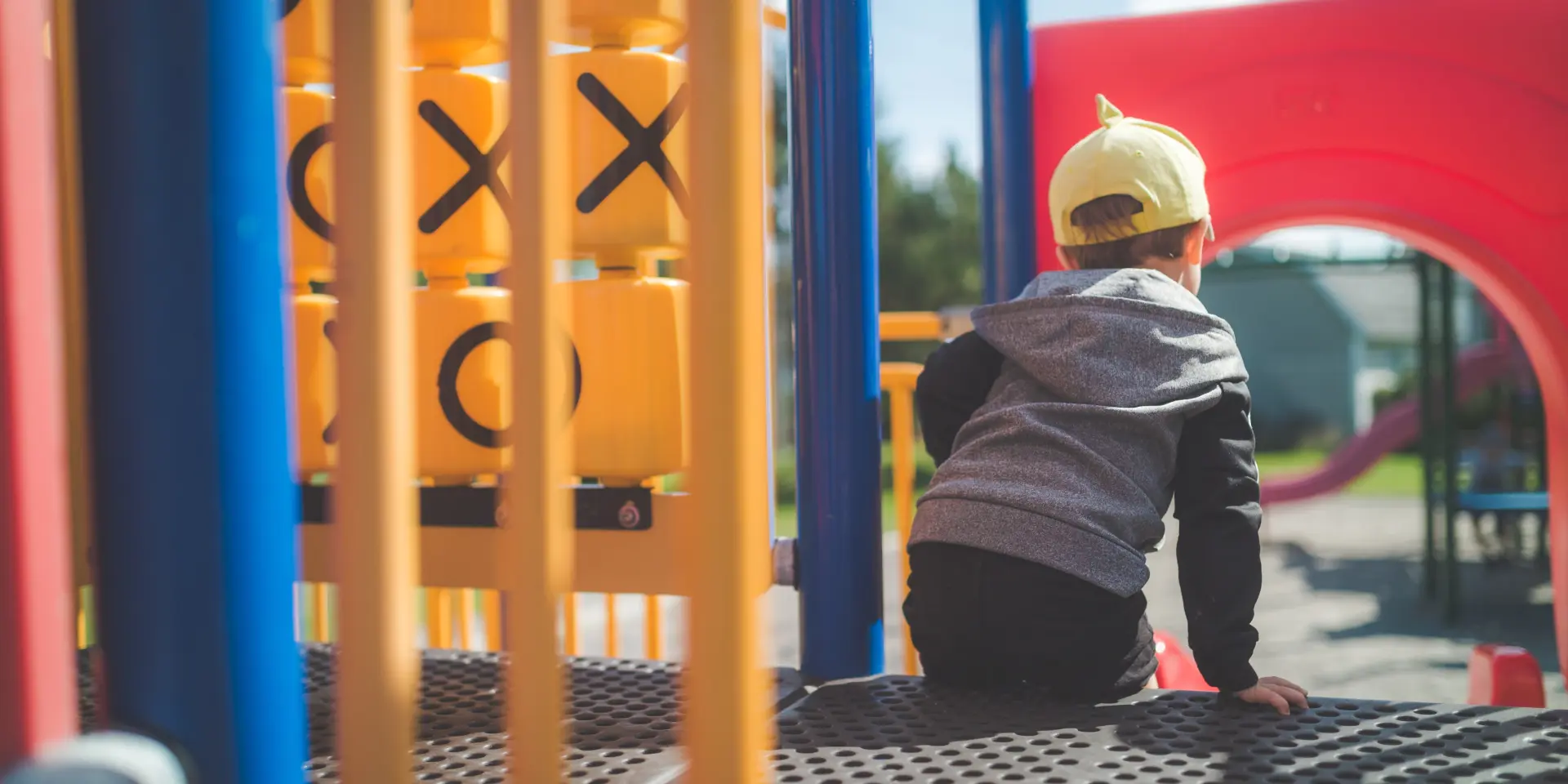 Un enfant portant un chapeau jaune est assis au sommet d'un toboggan dans une aire de jeux