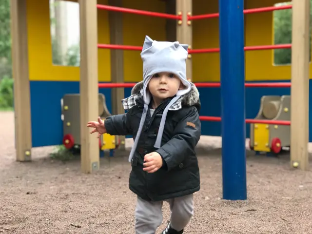 Enfant en manteau noir et chapeau gris jouant sur une aire de jeux colorée