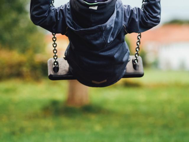 A child in a blue coat and gray hat on a swing in a park
