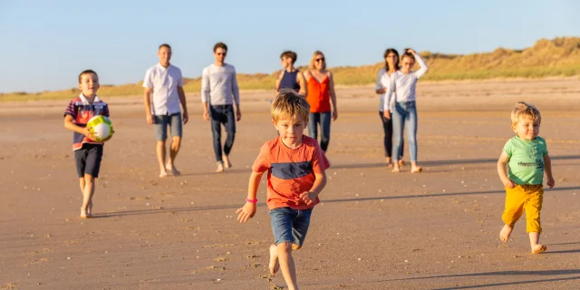 A group of children and adults playing with a ball on a sandy beach