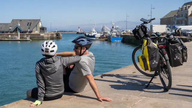 Two cyclists taking a break near a body of water with equipped bikes
