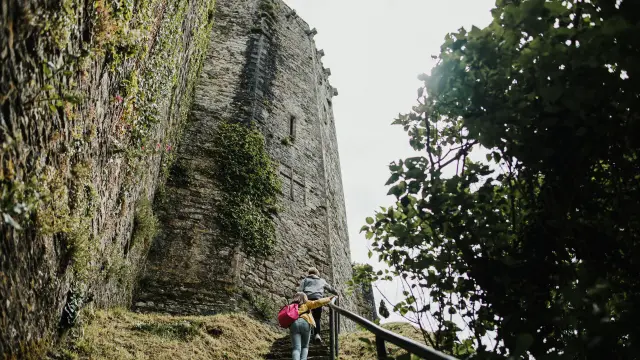 Two people climbing stairs towards a stone tower covered in vegetation