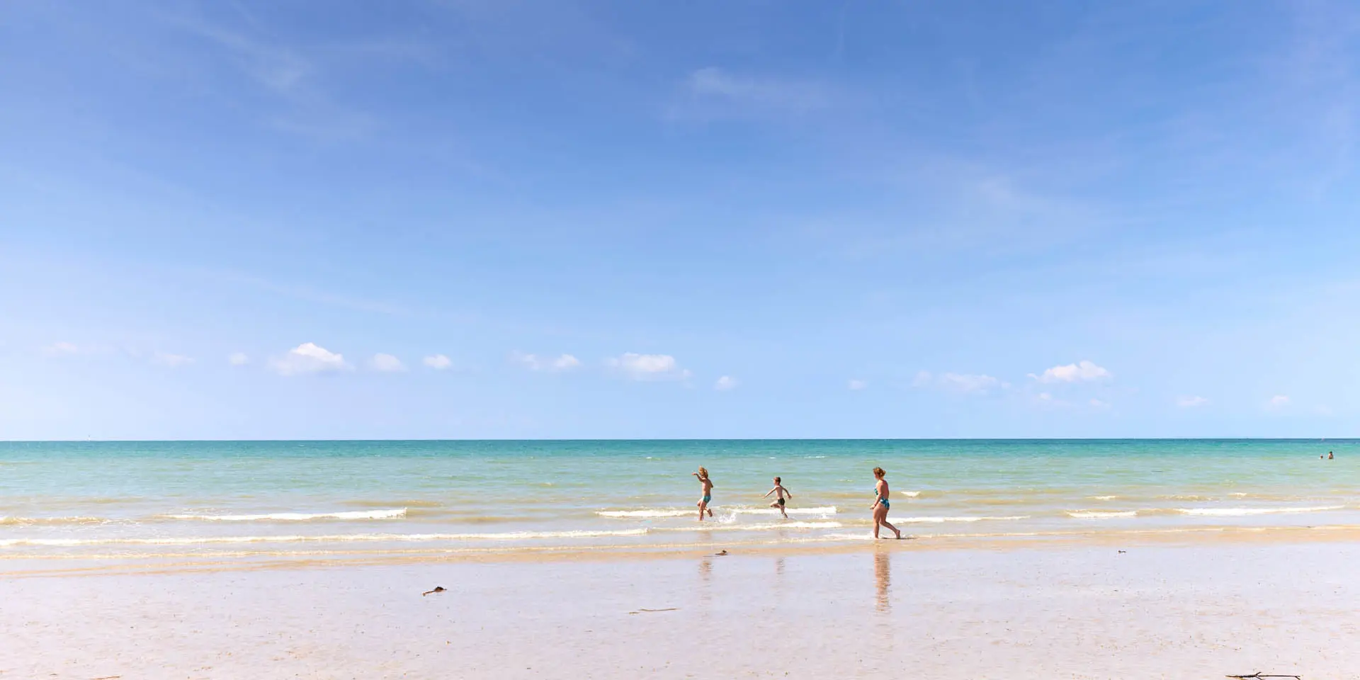 Drei Kinder laufen auf einem feinen Sandstrand