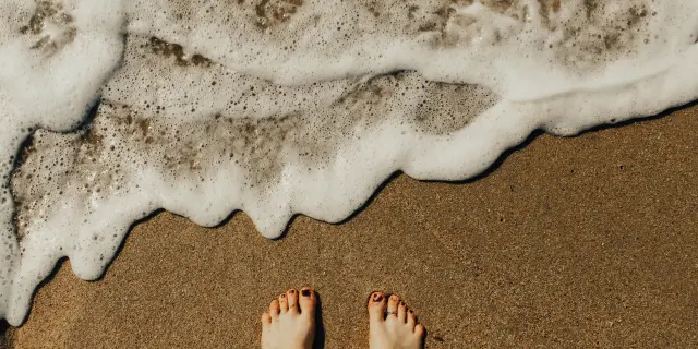 Zwei nackte Füße im Sand mit Wellen, die an Land spülen