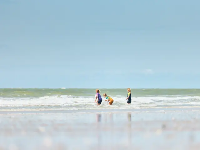 Trois enfants jouent dans les vagues sur une plage à Hauteville sur Mer