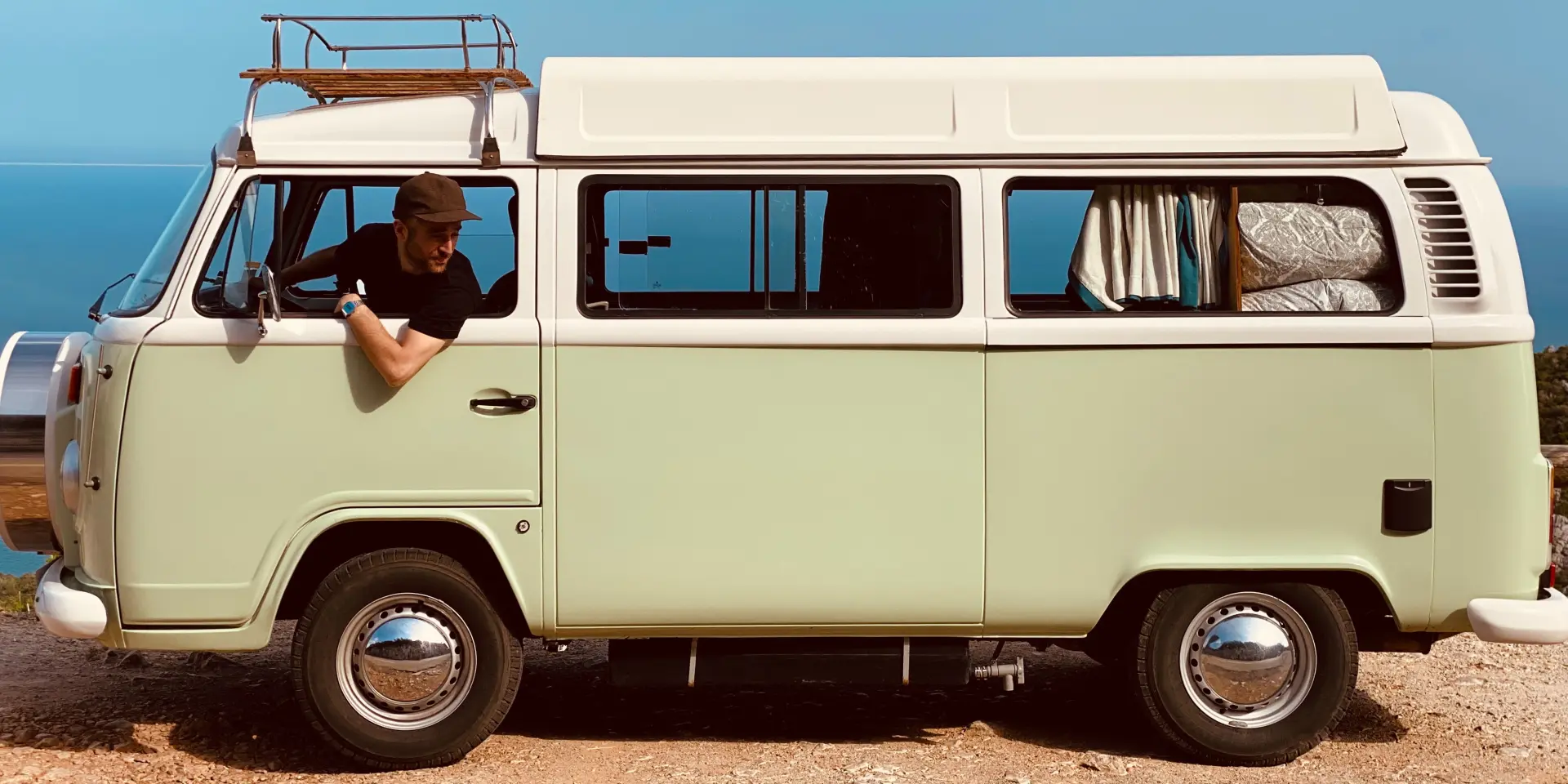 Un homme conduit un van vintage sur une route côtière