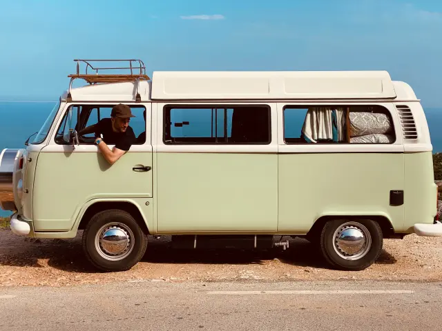 Un homme conduit un van vintage sur une route côtière