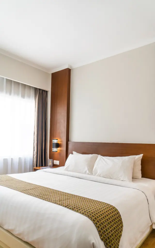Un lit double avec une couverture blanche et une couverture à motifs, des oreillers blancs et une tête de lit en bois