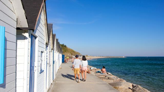 Deux personnes marchent le long d'une promenade en bord de mer avec des cabines de plage blanches à Carteret
