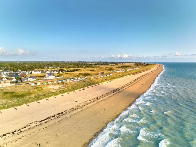A long sandy beach with houses and colorful beach cabins