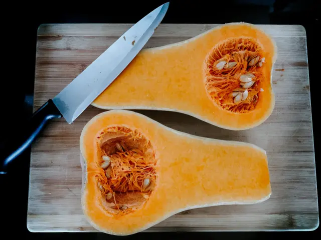 Deux moitiés de courge butternut sur une planche à découper avec un couteau
