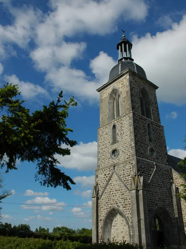 Tour d'église en pierre avec un ciel bleu et des nuages à Sourdeval Les Bois