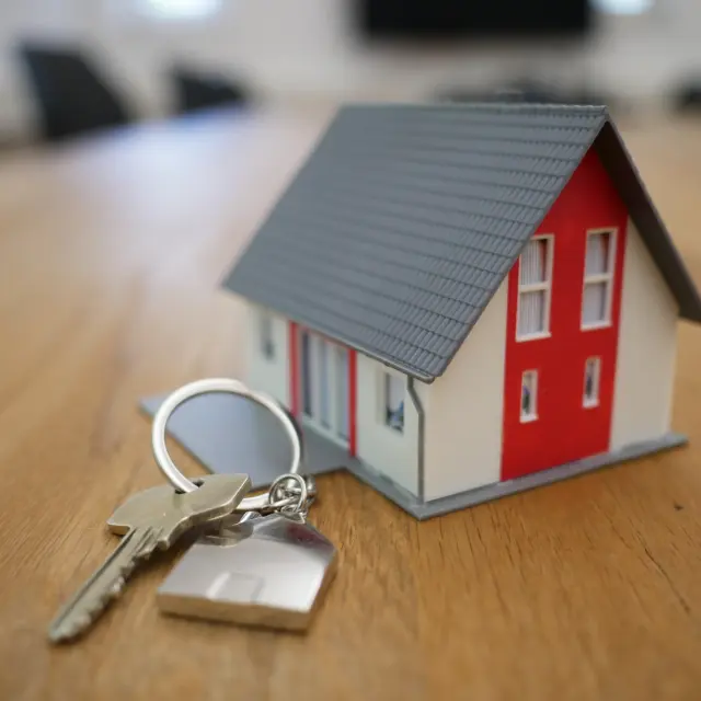 Une maison miniature rouge et blanche avec des clés à proximité