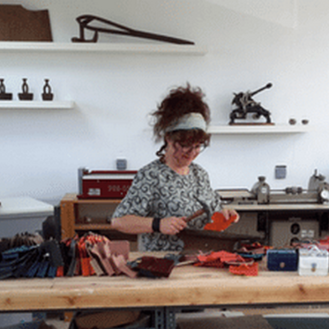Une personne travaillant sur un projet de couture dans un atelier rempli d'outils et de fournitures : Maroquinerie du Cotentin