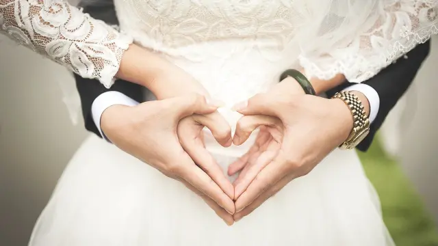 Deux mains formant un cœur sur le ventre d'une personne portant une robe de mariée