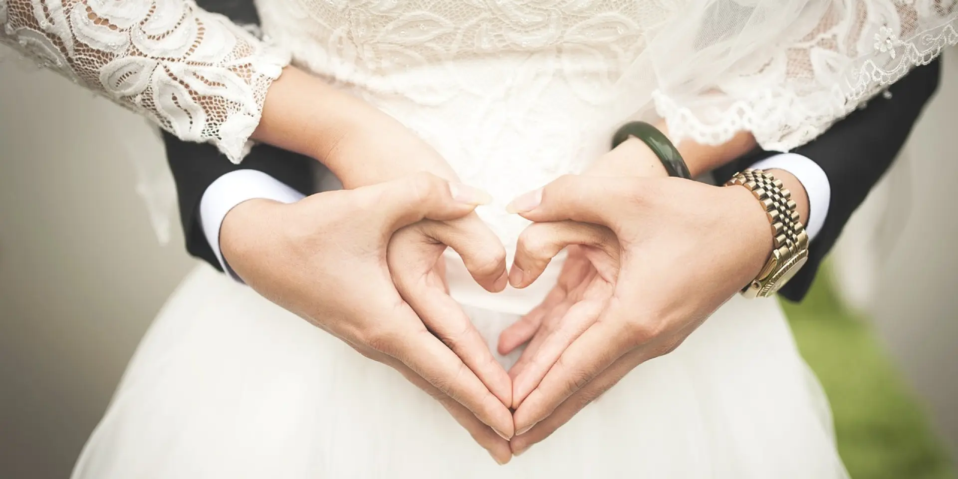 Deux mains formant un cœur sur le ventre d'une personne portant une robe de mariée