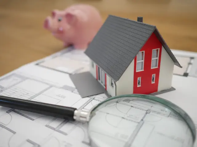 Maison miniature sur des plans de construction avec une loupe et un cochon tirelire