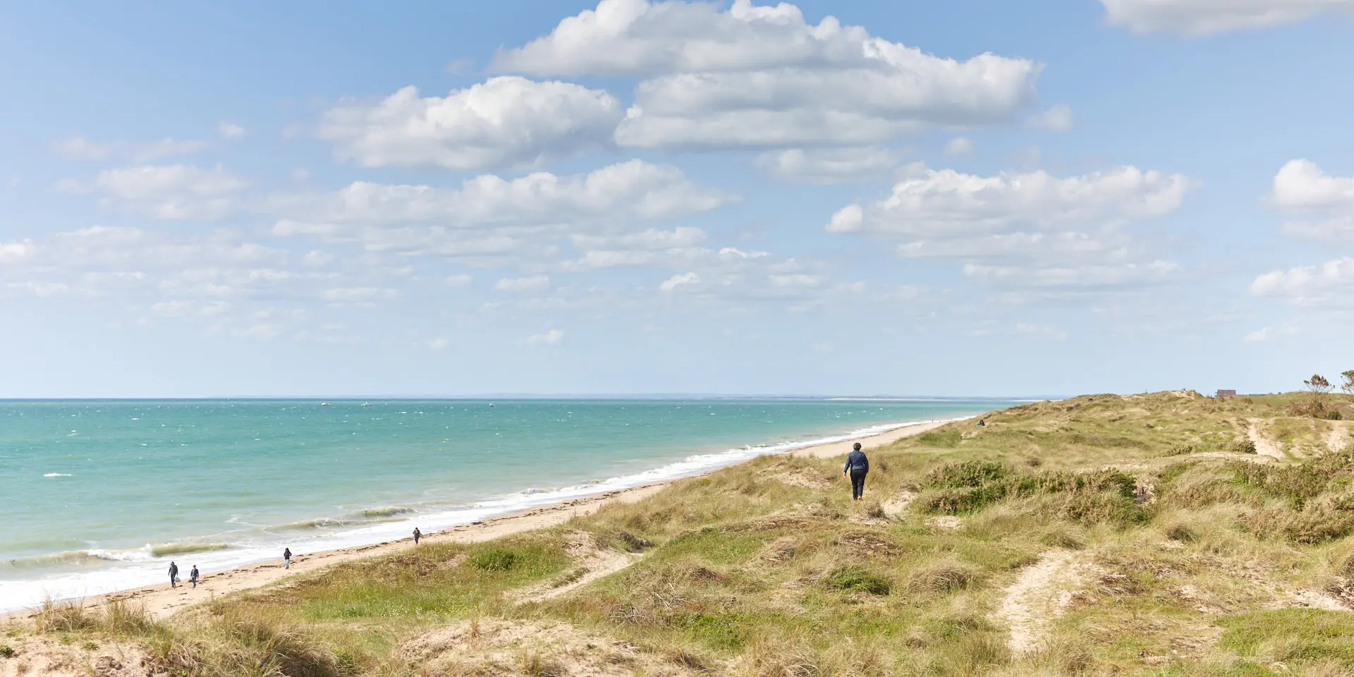 Personnes marchant sur une plage avec une mer bleue et un ciel nuageux