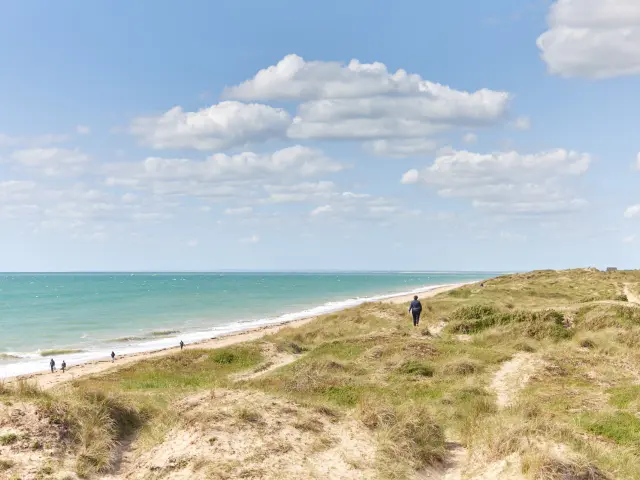 People walking on a beach with a blue sea and a cloudy sky