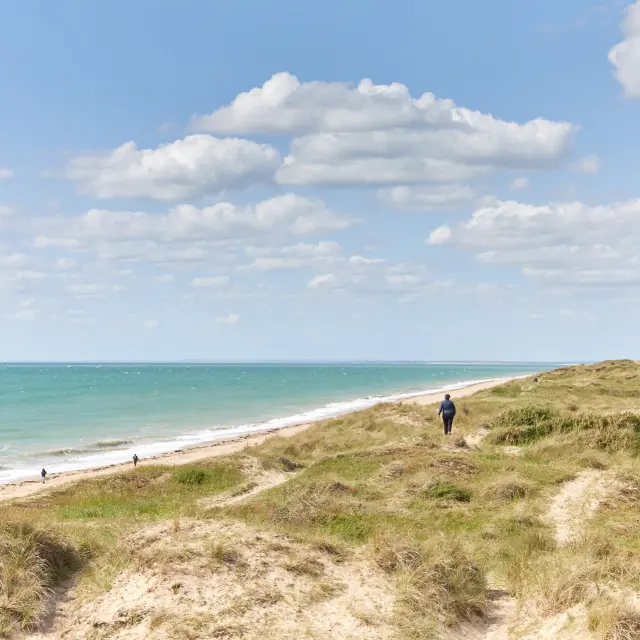 Personnes marchant sur une plage avec une mer bleue et un ciel nuageux