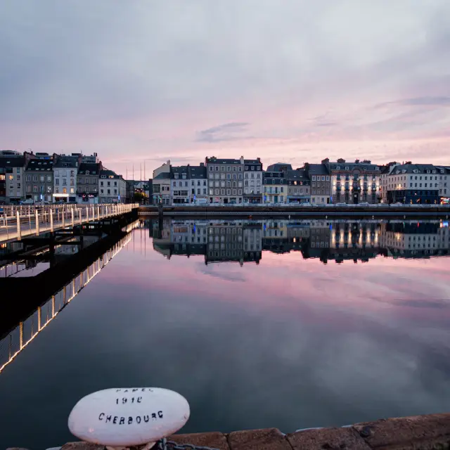 Port buoy with the inscription 'Cherbourg 1912' in front of buildings reflected in the water