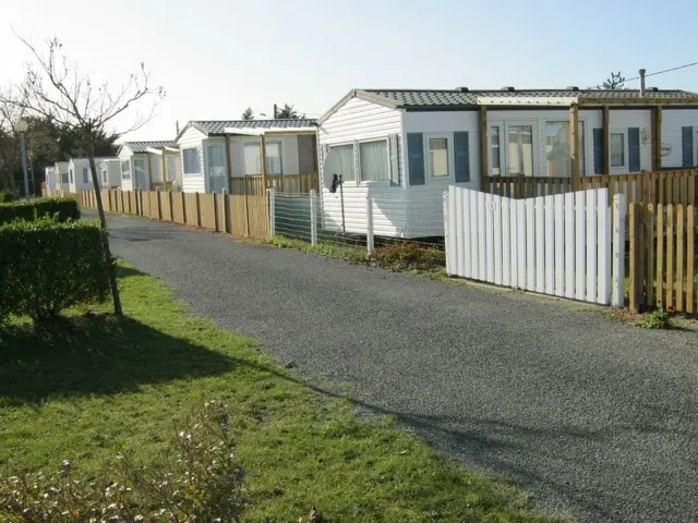 Une rangée de mobile homes avec des clôtures en bois et un chemin de gravier au camping de Hauteville sur Mer