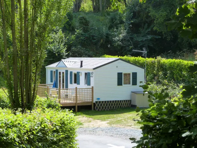 Un mobil-home blanc avec une terrasse en bois et des fenêtres bleues au camping de Coutances