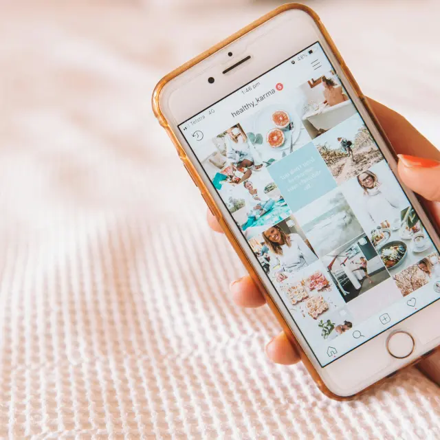 Main tenant un smartphone affichant le profil Instagram d'une utilisatrice