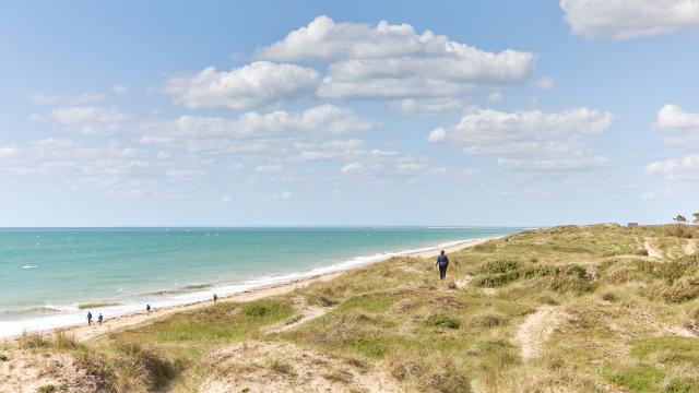 Personnes marchant sur une plage avec une mer bleue et un ciel nuageux