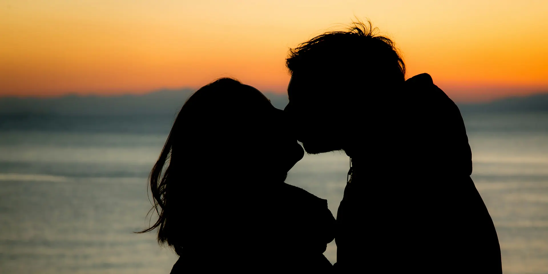 Deux silhouettes s'embrassent devant un coucher de soleil sur la plage