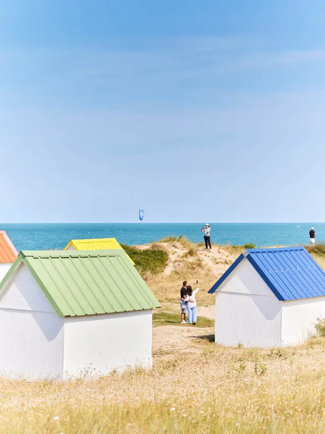Colorful beach huts with green, yellow, orange, and blue roofs near the sea