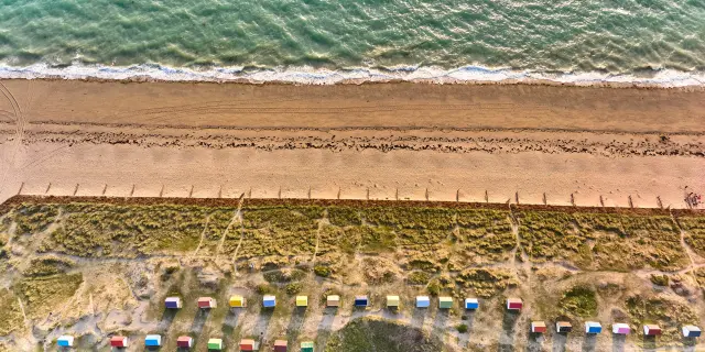 Aerial view of a beach with colorful beach huts and the ocean in the background
