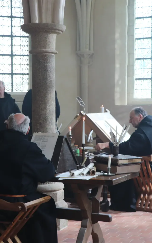 Des moines prient dans un monastère avec des chandeliers et des vitraux : reconstitution à l'Abbaye de Hambye