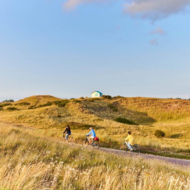 Trois personnes faisant du vélo sur un chemin de bord de mer proche des cabines de Gouville sur Mer