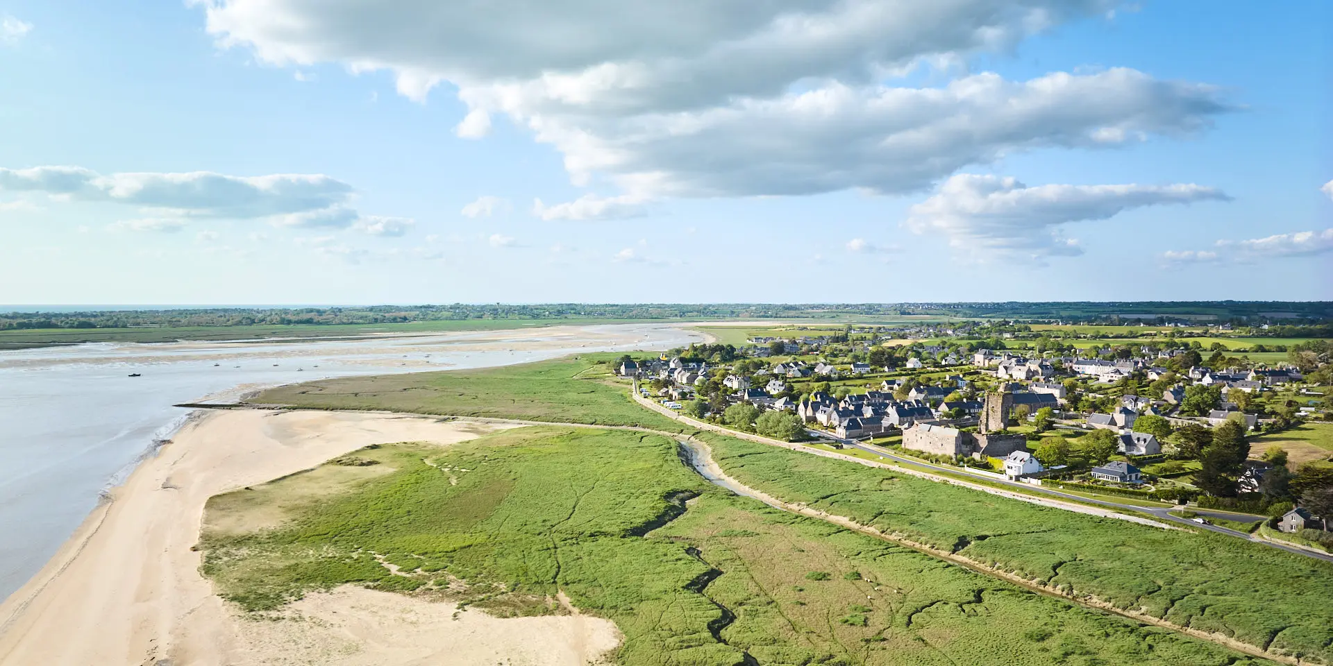 Vue aérienne d'un village côtier avec une plage déserte et des terres agricoles