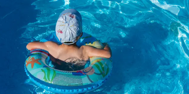Enfant portant un bonnet de bain et nageant avec une bouée en forme d'animal